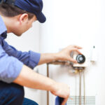 A repairman adjusts the temperature setting on a water heater.